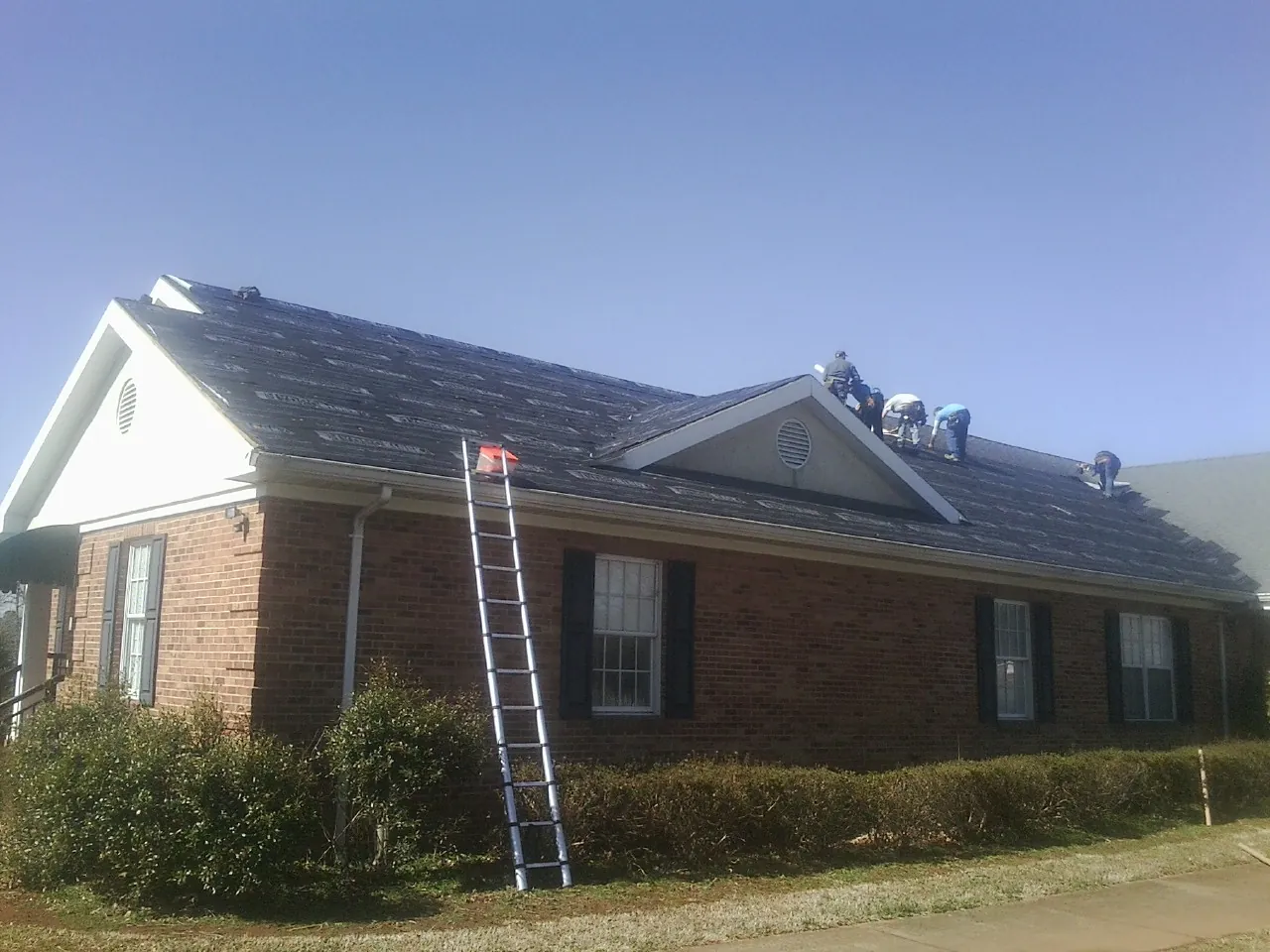 Crew tearing shingles off a brick ranch roof with a ladder set — Metal Roof Repair work by our crew in Frankfort