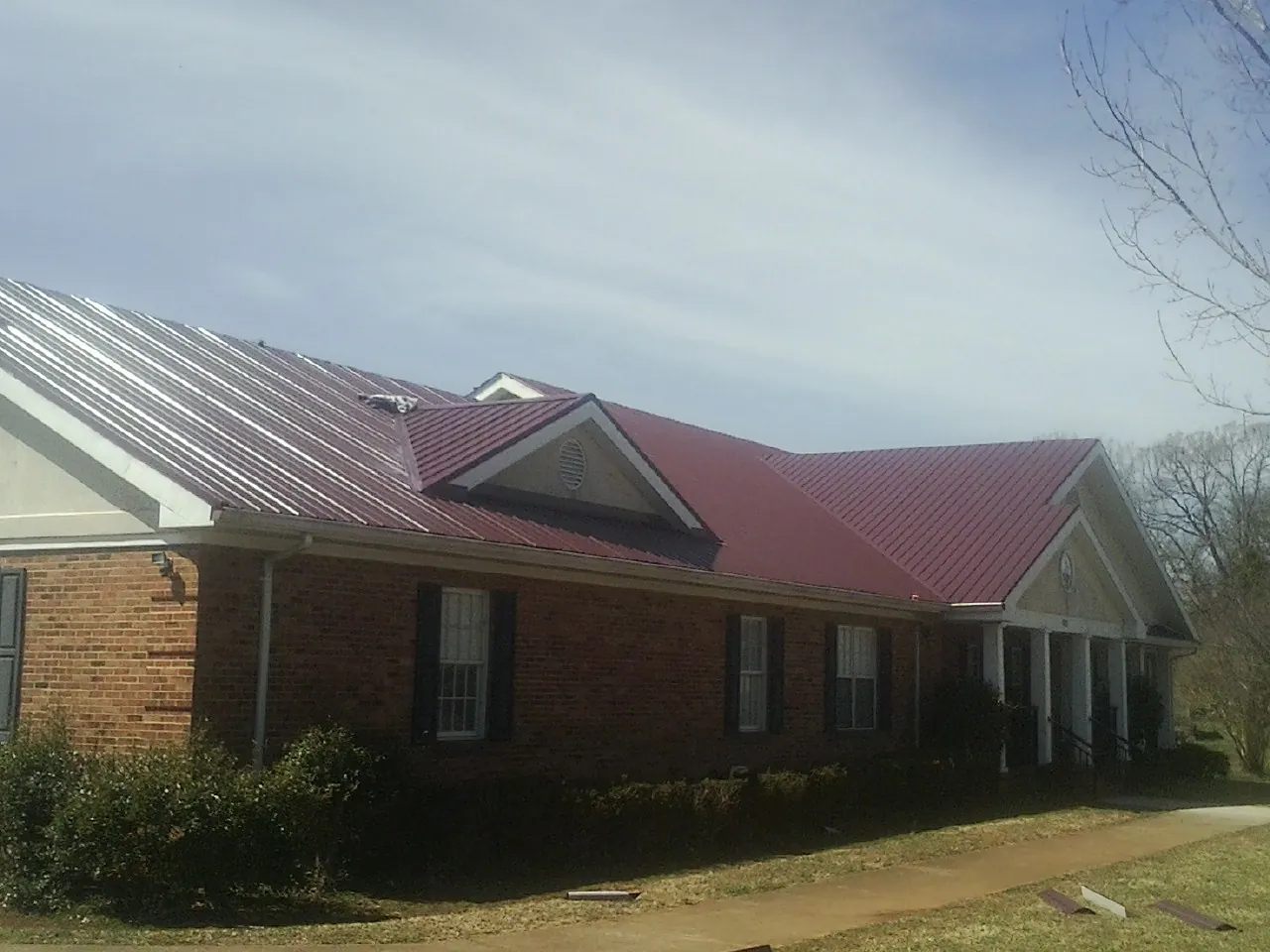 Red metal roof with gabled entries on a long brick building, from a Hail Damage Roof Repair job in Frankfort